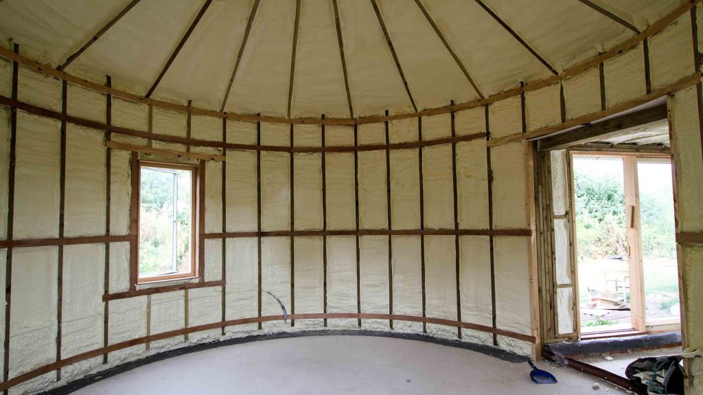 Spray foam lining the walls and roof of a converted steel grain silo, following every panel and rib.