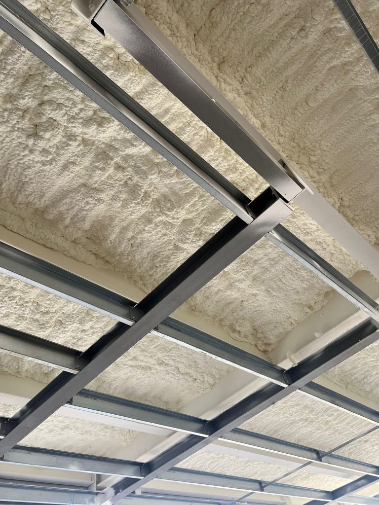 Closed-cell spray foam insulation to a steel deck soffit between structural beams.